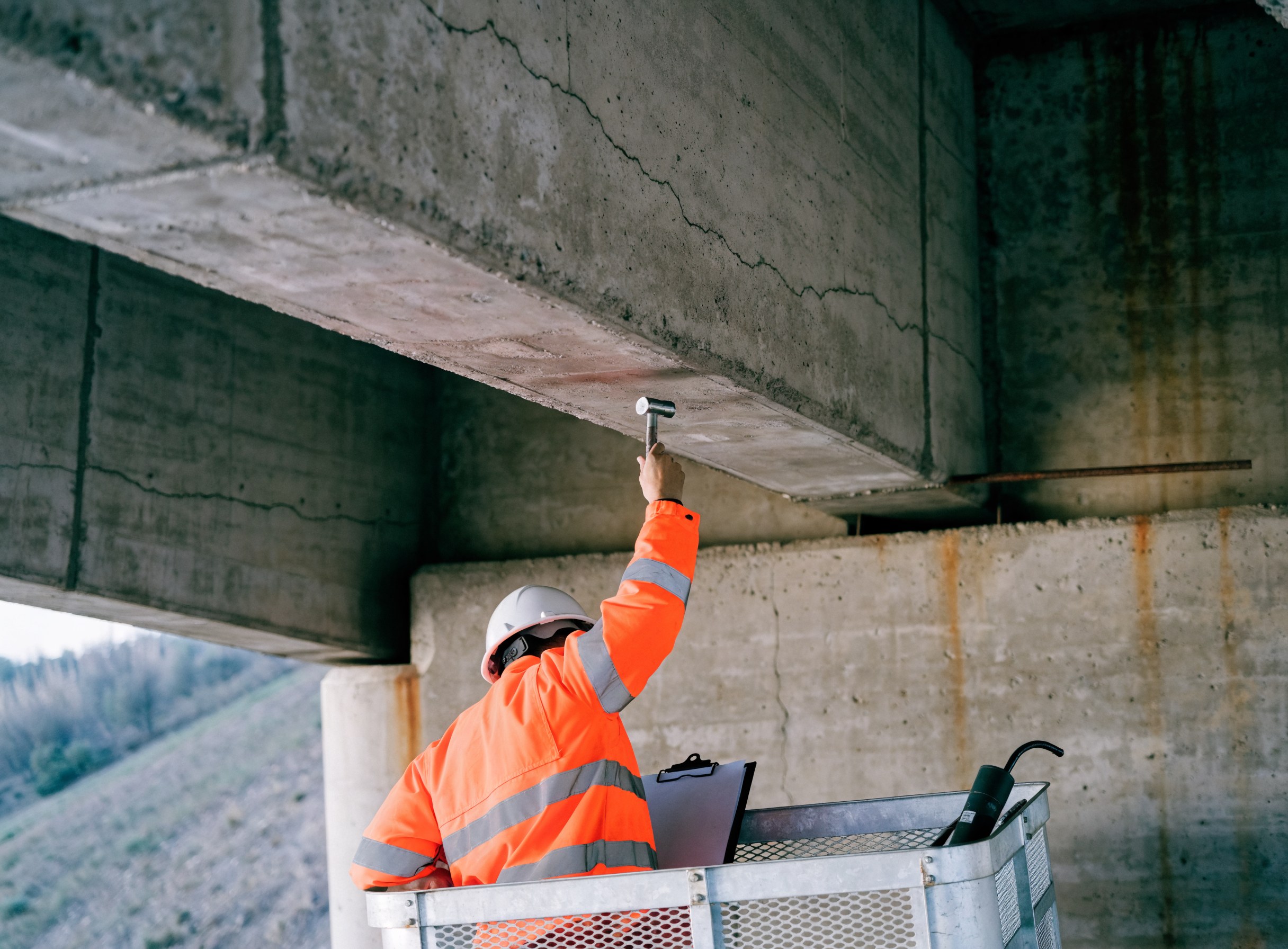 Prüfer im Arbeitskorb prüft handnah den Betonträger einer Brücke mit dem Hammer (KI-generierte Aufnahme)